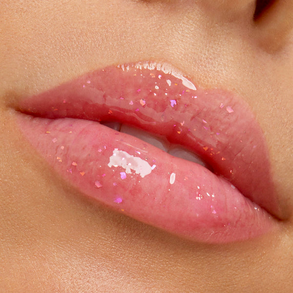 Glossy pink lips wear a sheer, iridescent flake gloss in a tight close-up, highlighting multidimensional sparkle from the Stranger Things x ColourPop Full Collection set and the ColourPop Ultra Glossy Lip.