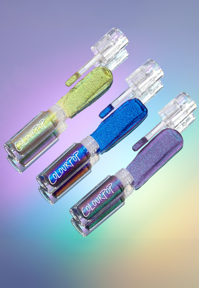 ColourPop multichrome liquid eyeshadows - three clear tubes with doe‑foot wands swatching shimmering lime, electric blue, and lavender shades - fanned on an iridescent gradient backdrop to showcase holographic payoff and sleek packaging.