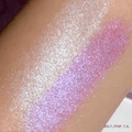 Moon Kingdom ColourPop Pressed Powder Highlighter swatches catching light on a forearm - an icy pearl stripe beside a lilac-to-pink duochrome - showing smooth, high-shine sparkle and buildable glow in a close-up makeup test.