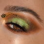 Shimmering green-gold eye makeup blends metallic lime on the lid into warm honey-brown matte, accented by a tiny bee graphic near the brow, on a close-up eye with long lashes, showcasing the Sweet As Can Bee Shadow Palette, a ColourPop Shadow Palette.