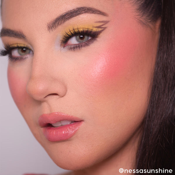 Model showcasing bold yellow eyeshadow with graphic black winged liner, fluttery lashes, rosy blush, and glossy pink lips, demonstrating the Pokémon x ColourPop Collection from the ColourPop Full Collection Set in a studio close-up.