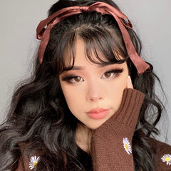 Model showcases a soft neutral eye using the ColourPop Gone Matte shadow palette, blending taupe-brown mattes with a smoky wing; wavy dark hair tied with a brown ribbon and a brown sweater with daisy embroidery in a studio close-up.
