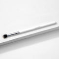 ColourPop Blending Brush makeup brush resting diagonally on a white textured surface, featuring fluffy angled black-to-white bristles, a silver ferrule, and a slim white handle, made for seamless eyeshadow blending.