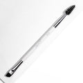 ColourPop Brow Dual Ended makeup brush resting diagonally, featuring an angled flat brow brush for filling and a black spoolie for grooming, white handle with chrome ferrules, on a bright white textured background.