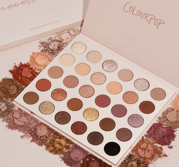 ColourPop Shadow Palette Bare Necessities lies open, showing 30 pressed neutral shades - matte and shimmer - ranging from ivory, taupe, and peach to bronze, plum, and black, arranged in rows amid scattered crushed pigments on a textured surface.
