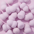 Hourglass Blending Sponge, lavender hourglass-shaped beauty sponges scattered on a pastel pink surface, featuring a double-curved design for smooth foundation and concealer blending; pairs well with ColourPop Makeup Tools & Accessories.