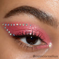 Individual ColourPop Crystal Face Jewels accent a brown eye, forming a dotted wing above shimmery pink eyeshadow with an inner-corner gem; iridescent adhesive rhinestones line the upper lid and outer edge, showcasing placement and sparkle.