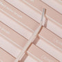 Brow Brush spoolie angling across stacked blush-pink ColourPop boxes, featuring a slim cream handle, twisted neck, and silver spiral bristles; a makeup brush designed to shape and feather brows.