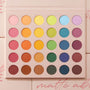 Crazy For Hue ColourPop Shadow Palette & Brush Set displays 30 matte rainbow shades arranged in a 5x6 grid - pinks, oranges, yellows, greens, blues, purples, and neutrals - set in a blush-pink case lying open on a soft pink background.
