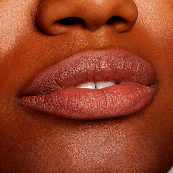 Full lips wearing All My BFFs, a warm rosy-brown nude ColourPop Lippie Pencil, lining and filling the mouth with a creamy satin finish on deep skin in a tight close-up, highlighting precise definition and smooth texture.