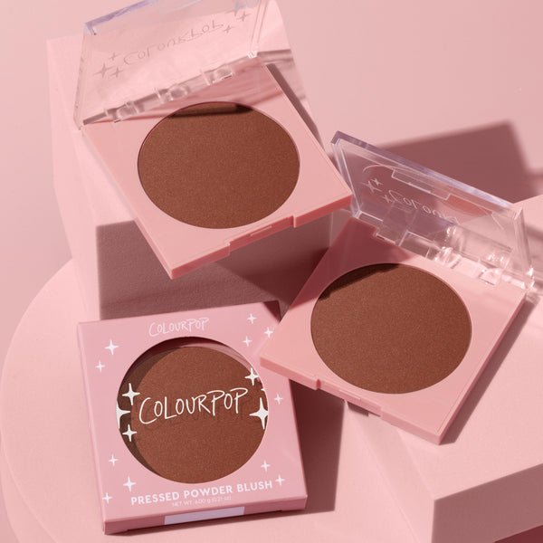 ColourPop Pressed Powder Blush in Full Throttle displayed as three pink square compacts - two open with clear lids revealing a warm terracotta pan, one boxed - arranged on pastel pink blocks under soft light.