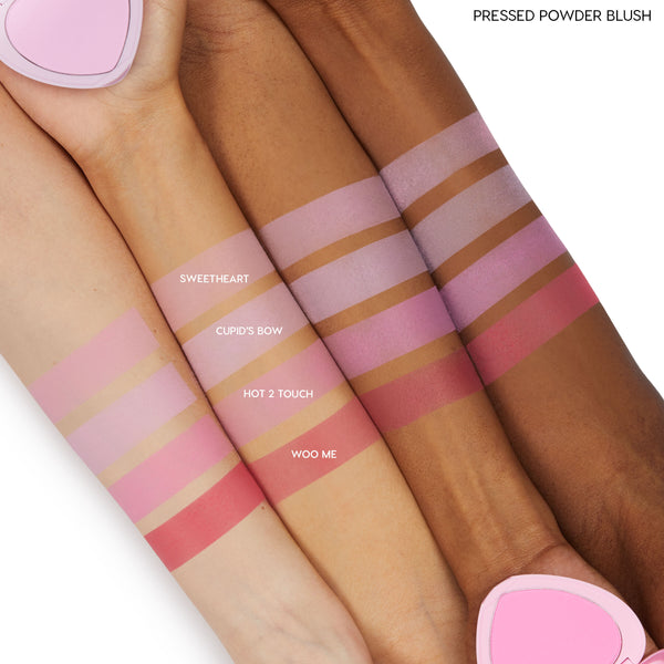ColourPop Pressed Powder Blush in Sweetheart swatched as a soft matte pink stripe across three arms in light, medium, and deep skin tones, shown alongside Cupid’s Bow, Hot 2 Touch, and Woo Me for comparison, with a pink heart compact at the edges.