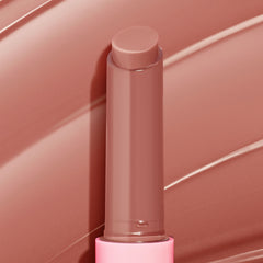 ColourPop So Juicy Plumping Gloss Balm with Peptides in Doe stands uncapped, twist-up stick revealing a creamy warm nude-brown tint, set against matching glossy swipes, in a pink tube for a plumping, glossy finish.