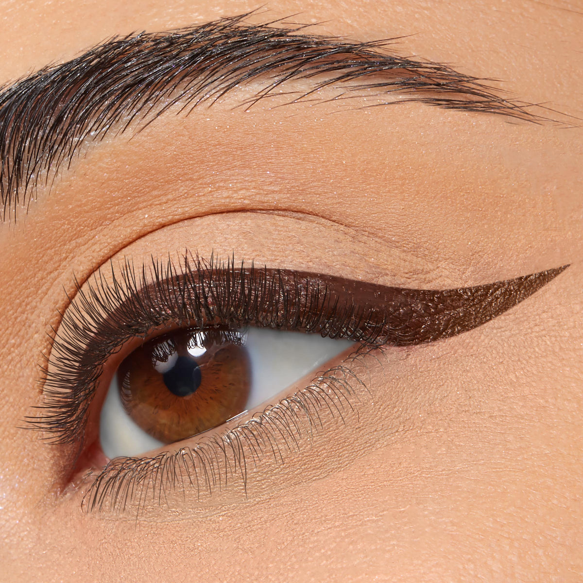 Winged eyeliner defines the upper lash line in a sharp, deep-brown cat eye, created with ColourPop BFF Liquid Liner in Grande, on a close-up of a brown eye with soft nude shadow and a groomed brow.