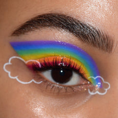 Rainbow winged eyeshadow sweeps from violet to red with white cloud liner below, created using the Fade Into Hue ColourPop Shadow Palette; close-up of one eye shows bold pigment, curled lashes, and a groomed brow on dewy skin.