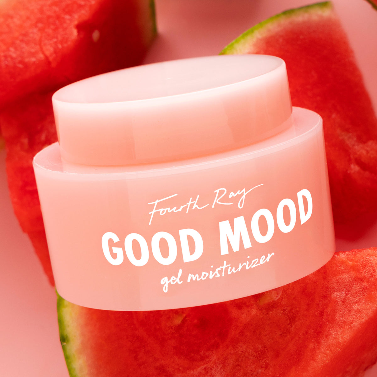 Pink jar of Fourth Ray Good Mood Gel Moisturizer by ColourPop angled on a pink surface, nestled among fresh watermelon slices, highlighting a lightweight gel face moisturizer; ColourPop Face Moisturizer for dewy hydration.