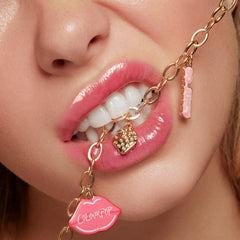 Brooklyn Charm x ColourPop Necklace dangling between glossy pink lips, a gold chain with enamel lip-shaped ColourPop charm, a gold strawberry pendant, and a pink “So Juicy” tag, studio close-up highlighting ColourPop Necklace details.
