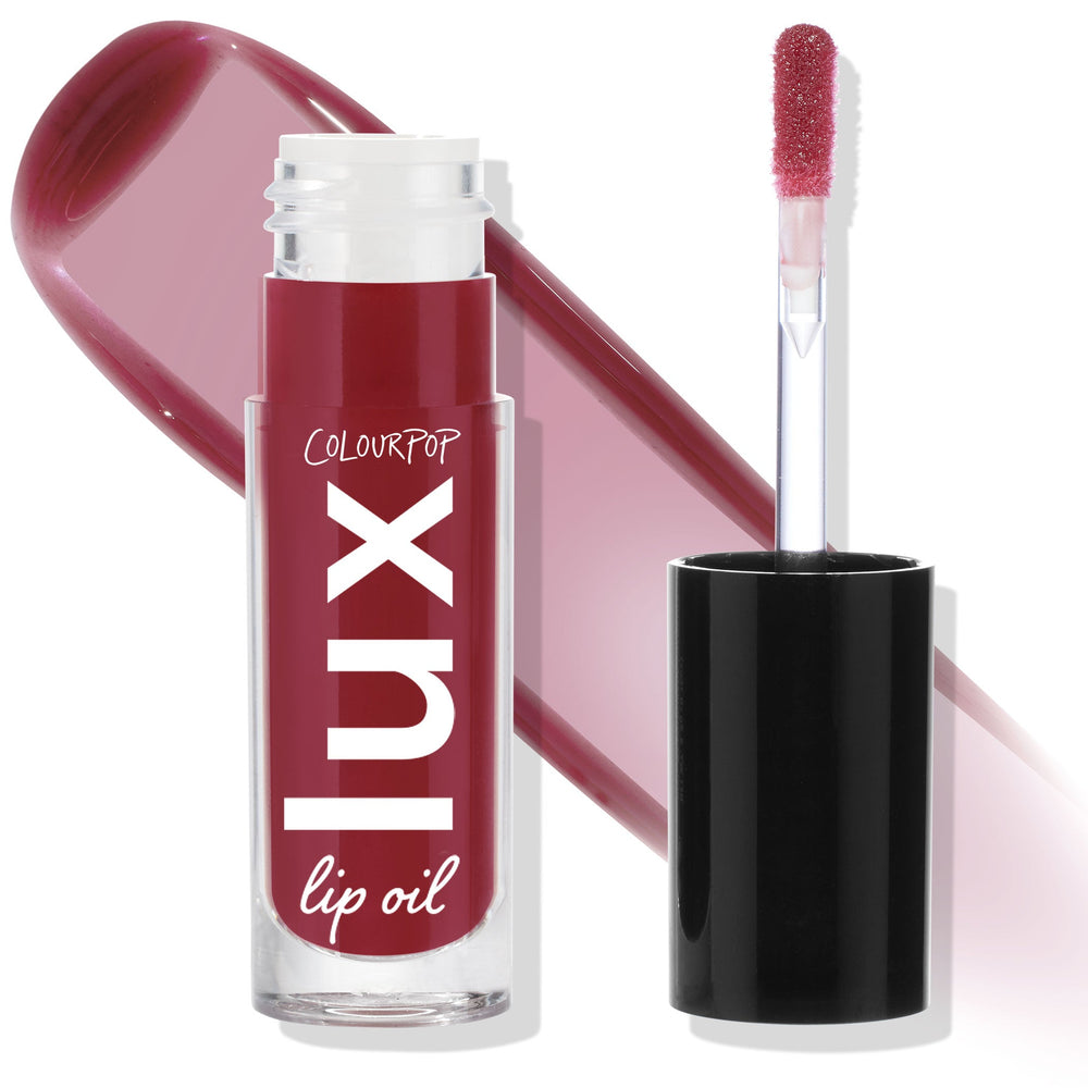 ColourPop Lux Lip Oil in Bells stands uncapped with a doe-foot applicator and black cap, showcasing a glossy berry-mauve tint; the clear tube displays Lux lip oil branding beside a matching swatch on a white background.