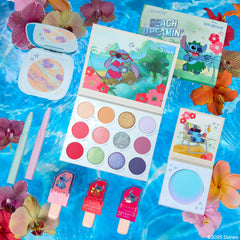 Disney Lilo and Stitch Collection full set by ColourPop displayed flat on a sparkling pool backdrop with orchids and hibiscus, featuring a 12-shade eyeshadow palette, pastel highlighters, two eye crayons, and three popsicle-shaped Ultra Glossy Lips.