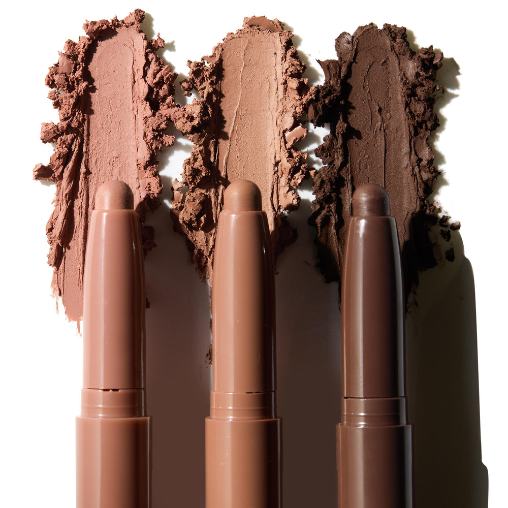 Three ColourPop Shadow Stix in Matte Nudes swipe creamy pigment, leaving wide matte swatches in light taupe, warm caramel, and deep cocoa on a white backdrop, with each twist-up eyeshadow stick aligned beneath its shade.