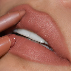 ColourPop Cookie Lippie Stix gliding onto lips, paired with a matching nude liner to define the cupid’s bow, showcasing a creamy warm beige-nude color in a tight close-up beauty shot.