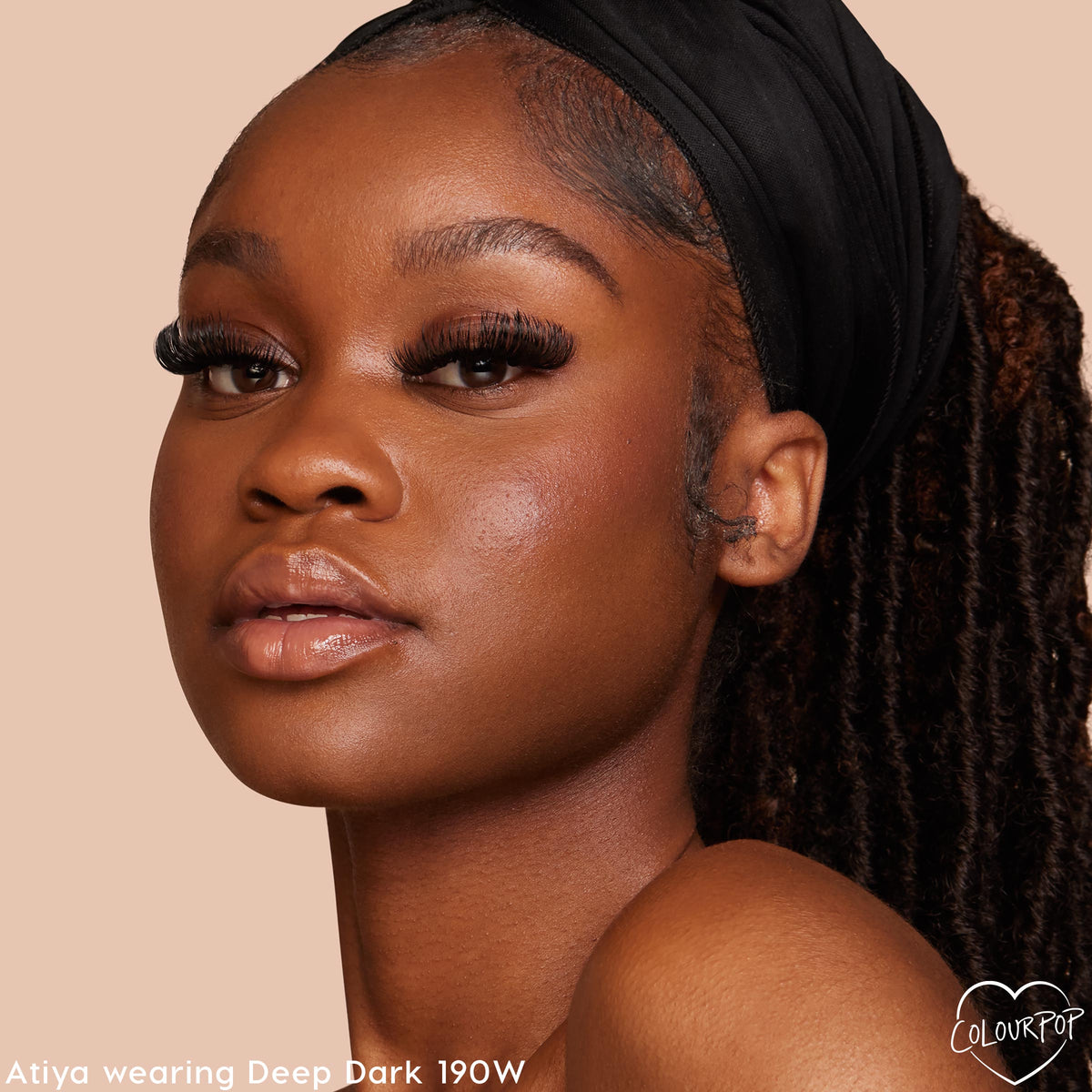 Model wearing ColourPop Hyaluronic Hydrating Foundation in Deep Dark 190 W, showcasing smooth, dewy coverage with warm undertones; close-up portrait with long lashes and glossy nude lip against a beige studio backdrop, ideal for deep skin.
