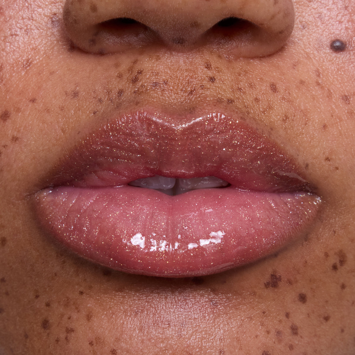 Close-up of freckled lips wearing Mademoiselle Belle Ultra Glossy Lip, a sheer pink Disney Princess lip gloss with high-shine, shimmery finish on medium skin tone, showcasing smooth, hydrated texture for beauty product detail.