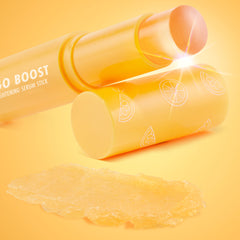 Ego Boost ColourPop Serum Stick uncapped, peach balm tip gleaming, yellow-orange tube labeled Brightening Serum Stick with citrus slice icons, and a creamy golden swipe of formula displayed on an orange gradient background.