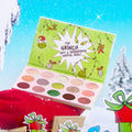 Colourpop How the Grinch Stole Christmas shadow palette opens to show matte and shimmer greens, pinks, and neutrals in festive Grinch artwork, staged on a snowy holiday scene with gifts.