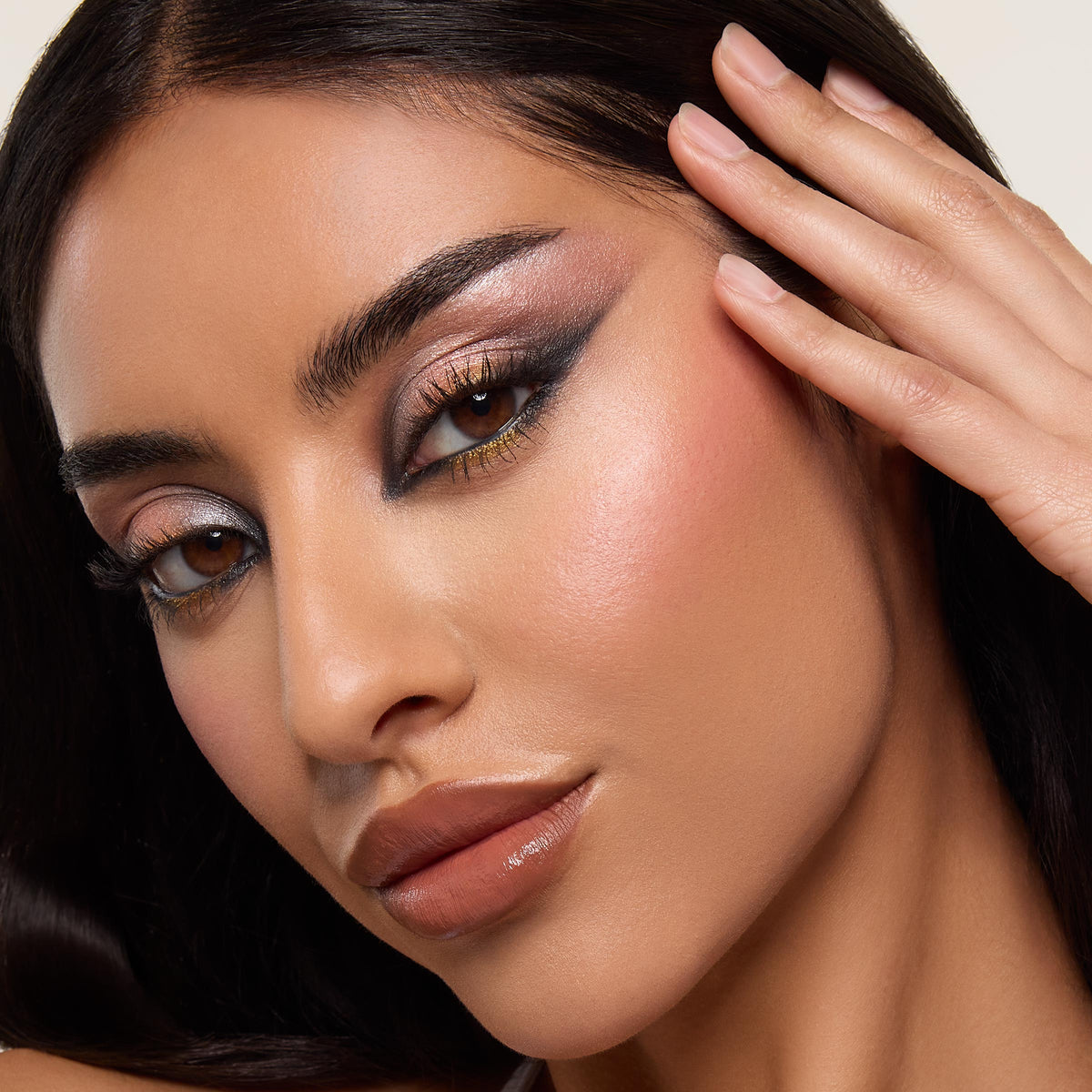 Metallic smoky eye look created with the ColourPop Shadow Palette, Precious Metals, blending shimmery rose, pewter, gold, and deep charcoal shades in a dramatic wing, shown in a close-up model face with hand at temple under soft studio lighting.