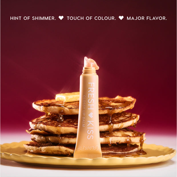 Colourpop Fresh Kiss Glossy Balm in Buttery Pancakes shade stands open with creamy gloss on the tip, propped against a syrupy pancake stack on a yellow plate, promoting Lip Gloss & Lip Oil with a hint of shimmer and flavor.