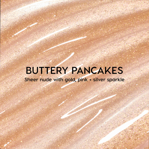 Colourpop Fresh Kiss Glossy Balm Buttery Pancakes swatch showing sheer nude lip gloss & lip oil texture with gold, pink, and silver sparkle streaked across a shimmery beige background, highlighting its high-shine finish.