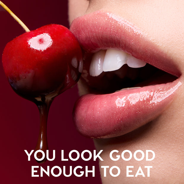 Close-up glossy pink lips wearing Colourpop Fresh Kiss Glossy Balm Chocolate Cherry shade parted near a chocolate-dipped red cherry against a deep red background, promoting luscious, juicy Lip Gloss & Lip Oil finish.