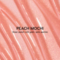 Colourpop Fresh Kiss Glossy Balm in Peach Mochi swatched in smooth, wavy streaks, showing a sheer peach Lip Gloss & Lip Oil texture with fine gold and pink sparkle against a close-up shimmering background.