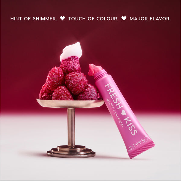 Colourpop Raspberry Crème Fresh Kiss Glossy Balm tube oozing pink shimmer next to a pedestal piled with fresh raspberries and whipped cream, highlighting juicy Lip Gloss & Lip Oil shine against a rich berry gradient background.