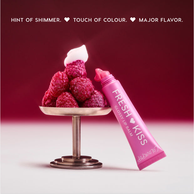 Colourpop Raspberry Crème Fresh Kiss Glossy Balm tube oozing pink shimmer next to a pedestal piled with fresh raspberries and whipped cream, highlighting juicy Lip Gloss & Lip Oil shine against a rich berry gradient background.