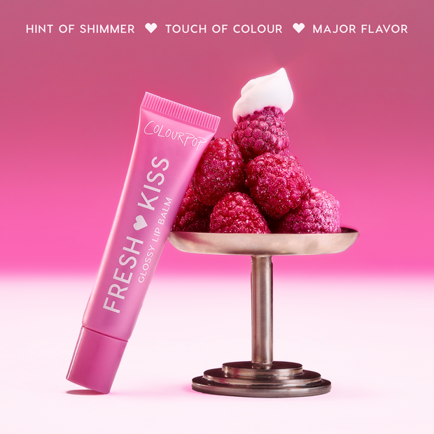 Colourpop Raspberry Crème Fresh Kiss Glossy Balm tube oozing pink shimmer next to a pedestal piled with fresh raspberries and whipped cream, highlighting juicy Lip Gloss & Lip Oil shine against a rich berry gradient background.
