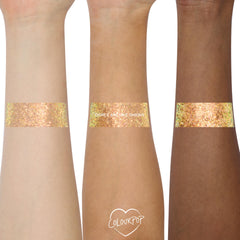 Wide swatches of ColourPop Glitter Gel, Ogres are Like Onions, brushed across three forearms to show payoff - peachy gold chunky hex glitter with a green iridescent shift and high sparkle - shot close-up on a clean white studio background.