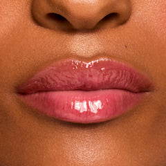 Glossy pink lips wearing a shade from the Fruit Basket ColourPop Glossy Lip Balm Trio, showing a sheer tint and high-shine, hydrated finish in a tight macro close-up on medium-brown skin.
