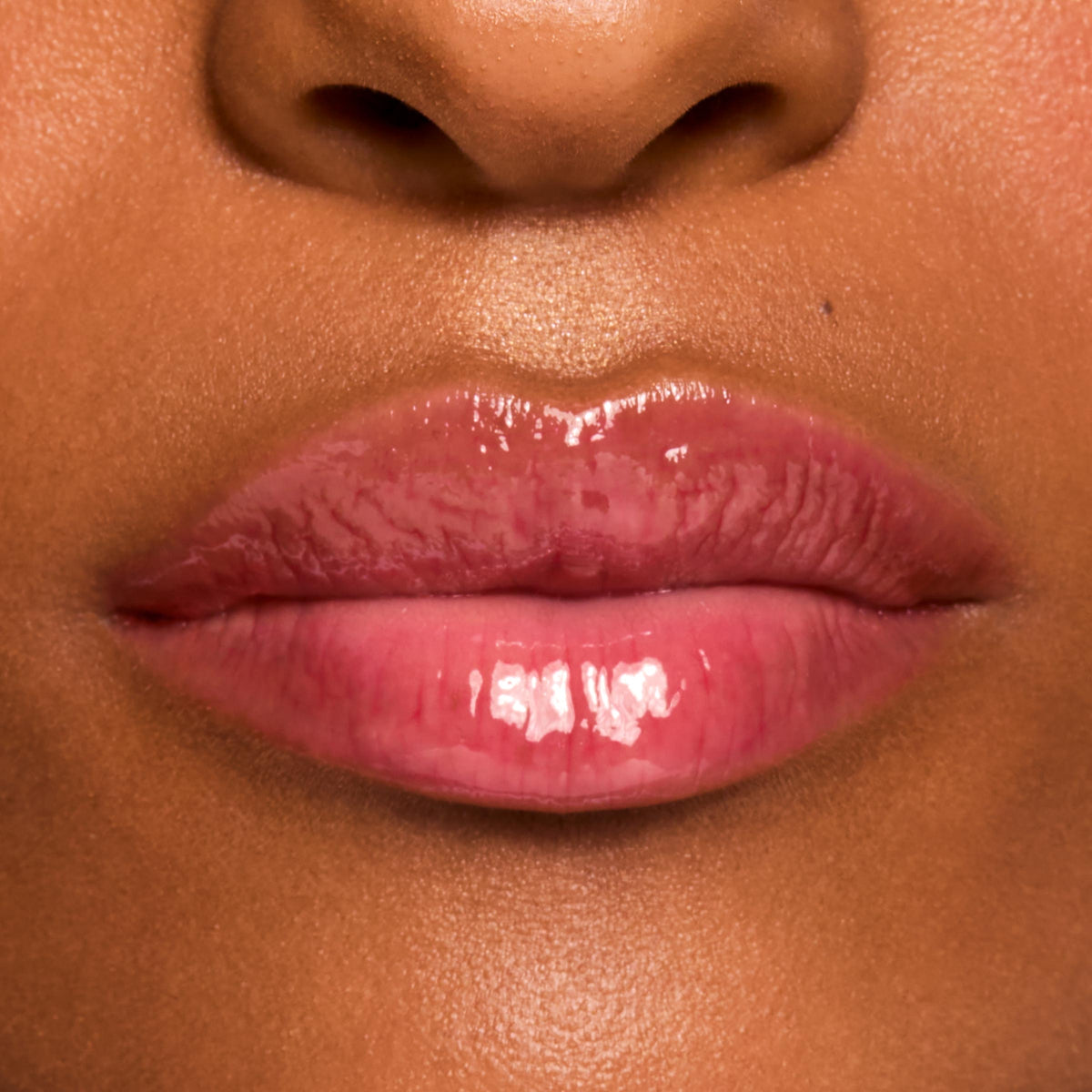 Glossy pink lips wearing a shade from the Fruit Basket ColourPop Glossy Lip Balm Trio, showing a sheer tint and high-shine, hydrated finish in a tight macro close-up on medium-brown skin.