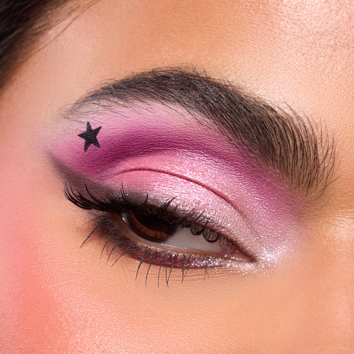 Close-up of a medium-skin eye with hot pink shadow and a stamped black star from the Best of Both Worlds palette