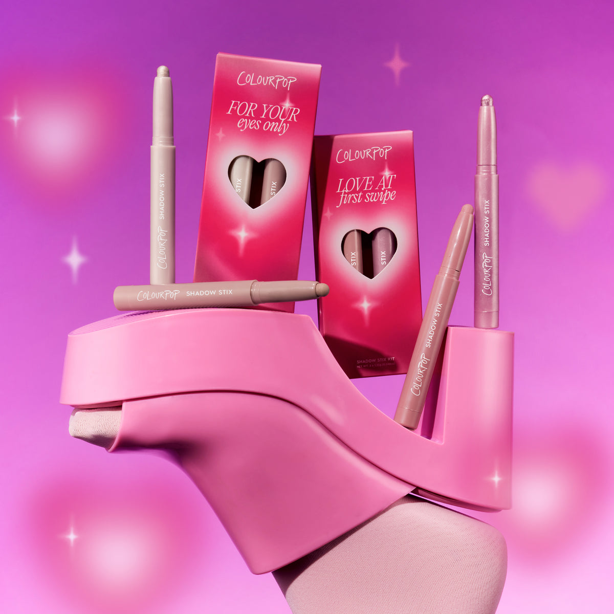 ColourPop All Eyes On Me Shadow Stix Set from the Heart to Get collection balanced on a bright pink platform heel, showing multiple nude-toned shadow sticks and heart-cutout boxes against a dreamy pink gradient background with sparkles.