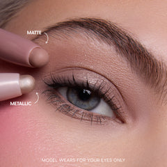 Close-up of a fair-skinned model’s blue eye wearing shimmery neutral shadow created with the All Eyes On Me Heart to Get Shadow Stix Set, showing matte and metallic cream eyeshadow tips applying blendable color on the eyelid.