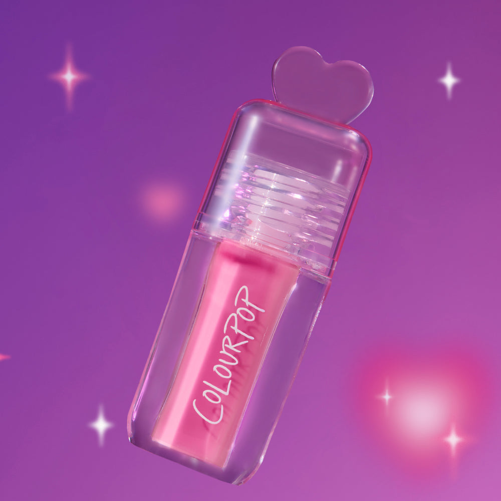 Heart to Get Text Me, JK blush + UGL set with a hot pink ColourPop stick encased in a clear heart-topped tube, floating against a dreamy purple background with soft sparkles, styled for a playful US beauty product shot.