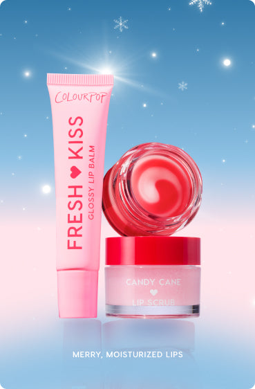 Colourpop Fresh Kiss Glossy Lip Balm tube, an open red‑swirled balm pot, and a Candy Cane Lip Scrub jar arranged upright against a blue‑to‑pink winter backdrop with snowflakes, showcasing a festive hydrating lip care set.