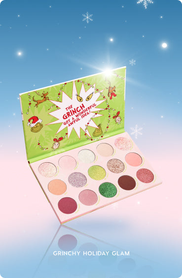 Colourpop Grinchy Holiday Glam eyeshadow palette opened to show 15 shimmery and matte pink, green, gold, and neutral pans, set against a pastel winter sky background with snowflakes for festive holiday makeup looks.