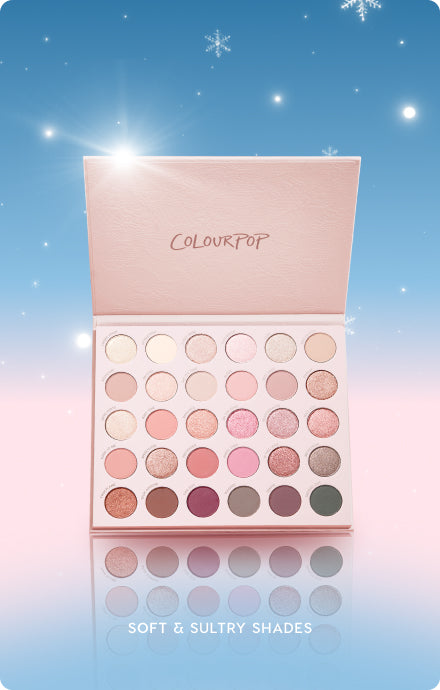 Colourpop eyeshadow palette stands open to reveal 30 soft and sultry neutral, pink, and shimmer shades, reflecting on a glossy surface against a pastel blue and pink holiday sky with snowflakes, perfect for festive makeup looks.