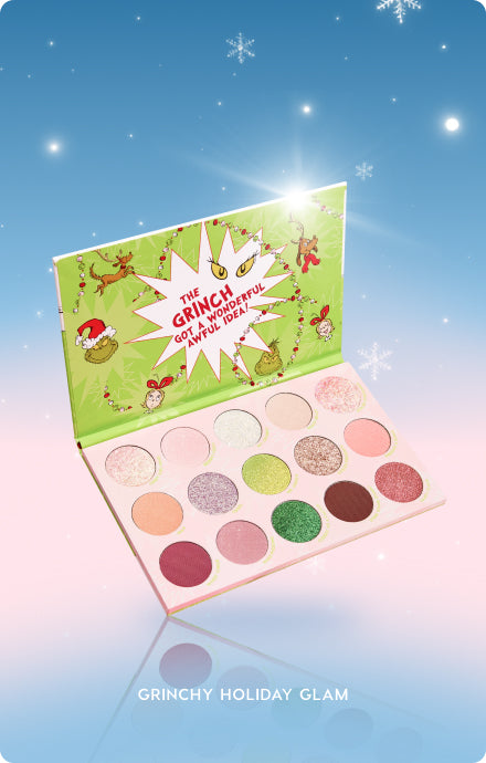 Colourpop The Grinch holiday eyeshadow palette lies open, displaying 15 matte and shimmer shades in pinks, golds, greens, and burgundies; lime‑green lid shows The Grinch and “got a wonderful awful idea,” set against a snowy blue‑to‑pink gradient background.