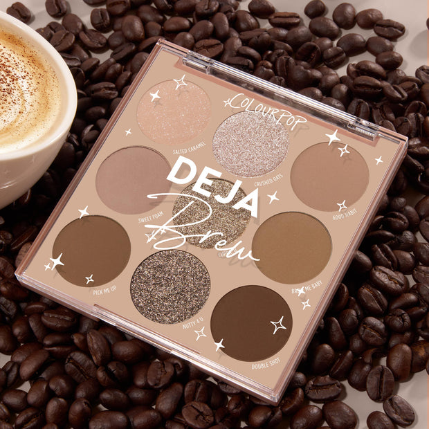 Deja Brew ColourPop Shadow Palette displaying nine coffee-inspired shades - matte and shimmer browns, taupes, and champagne - opened in a 3x3 layout on roasted coffee beans next to a latte, highlighting neutral eye looks.