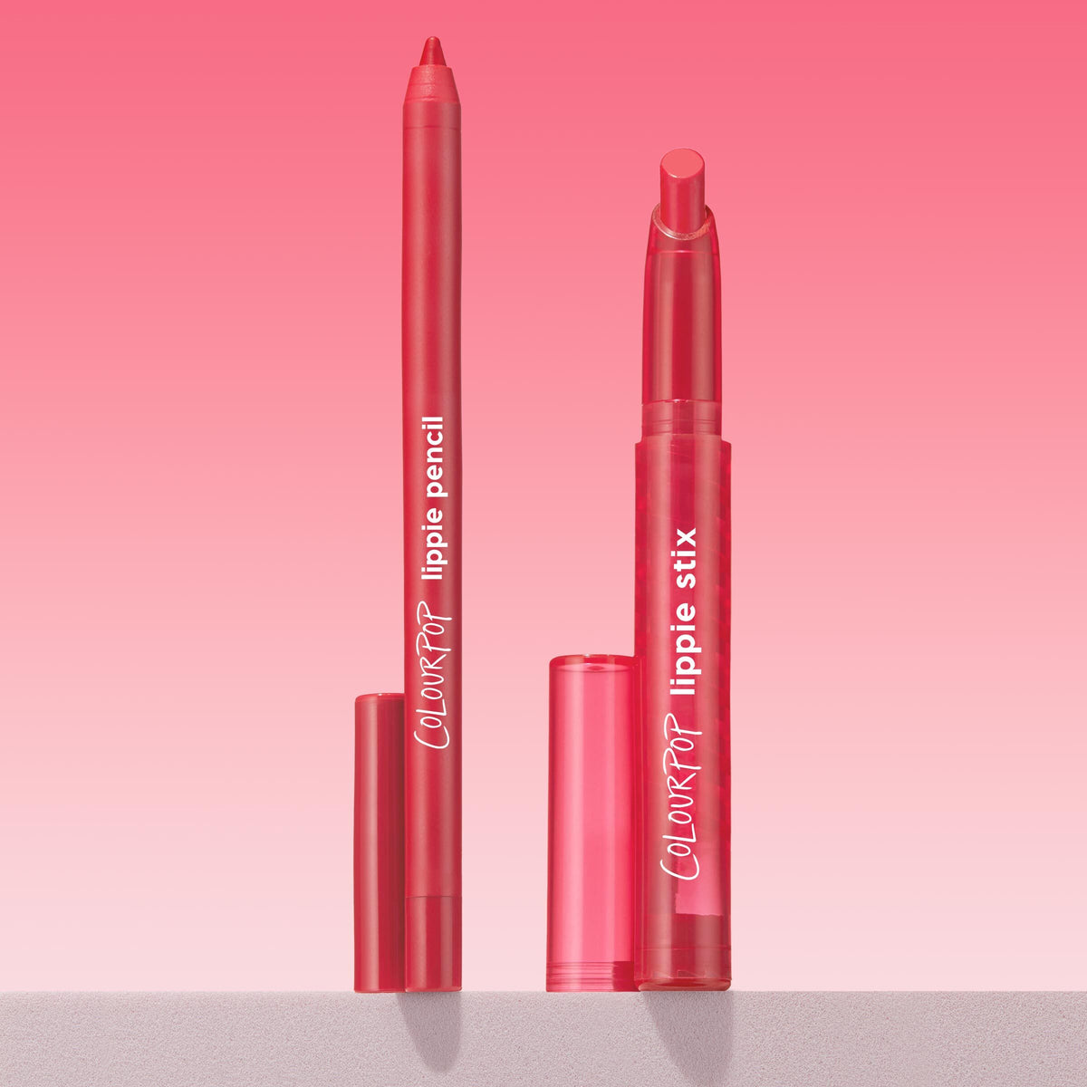 Bossy ColourPop Lippie Pencil defines lips in a bold red as a matching Lippie Stix lays down creamy color, both uncapped and standing upright with caps at the base on a pink gradient backdrop, showcasing the precise pencil tip and stix bullet.